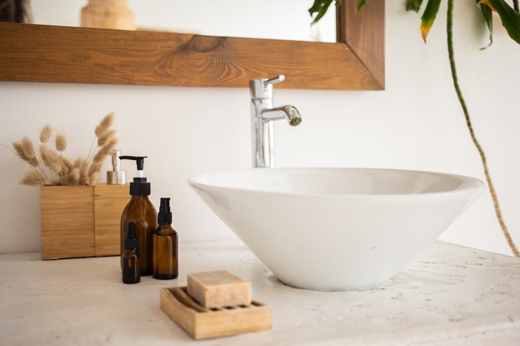 interior of bathroom table with soap and cosmetic oil placed near white sink and faucet under mirror in wooden frame in modern apartment